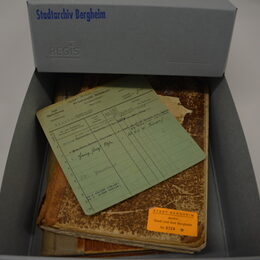 Geöffneter Archivkarton mit verschiedenen Archivalien, obenauf eine Alphabetische Meldekarte